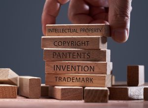 man adding a block showing the words ’Intellectual property’ on top of other wooden block with text copyright, patents, invention,and trademark