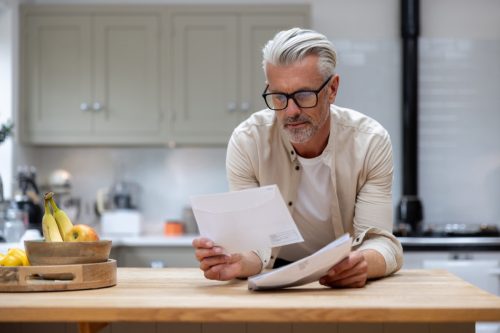 white-haired man looking at mail in his kitchen