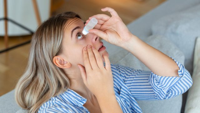 woman putting in eye drops at home