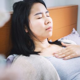 A woman lying in bed with a pained look on her face while touching her chest, possibly feeling discomfort from heartburn