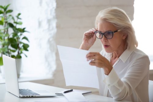 older woman looking at a piece of paper in front of her laptop