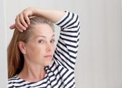 Beautiful 40s woman looking at gray hair in mirror reflection on growing out root