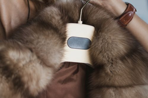 Close up of a woman's hand grabbing the hanger on which a brown, fur-lined winter jacket hangs
