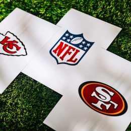 Chiefs and 49ers logos, along with an NFL logo, on white papers sitting on grass