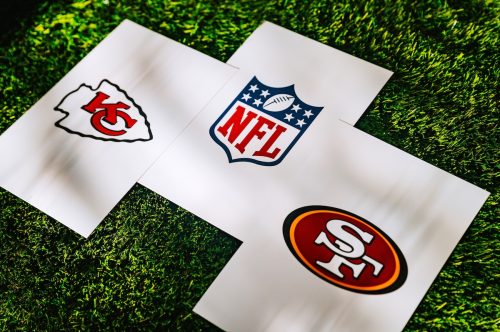 Chiefs and 49ers logos, along with an NFL logo, on white papers sitting on grass