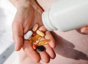 Closeup photo of supplements with a white bottle. Pregnant woman take omega 3, multivitamins, vitamins B, C, D, collagen tablets, probiotics, iron capsule. Girl hold vitamins daily. Top view.