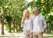 Romantic Senior Couple Walking Outdoors In Summer Park And Embracing, Loving Happy Mature Spouses Hugging And Smiling To Each Other, Cheerful Husband And Wife Enjoying Outside Walk, Copy Space