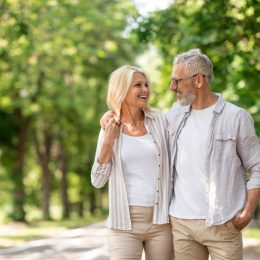 Romantic Senior Couple Walking Outdoors In Summer Park And Embracing, Loving Happy Mature Spouses Hugging And Smiling To Each Other, Cheerful Husband And Wife Enjoying Outside Walk, Copy Space
