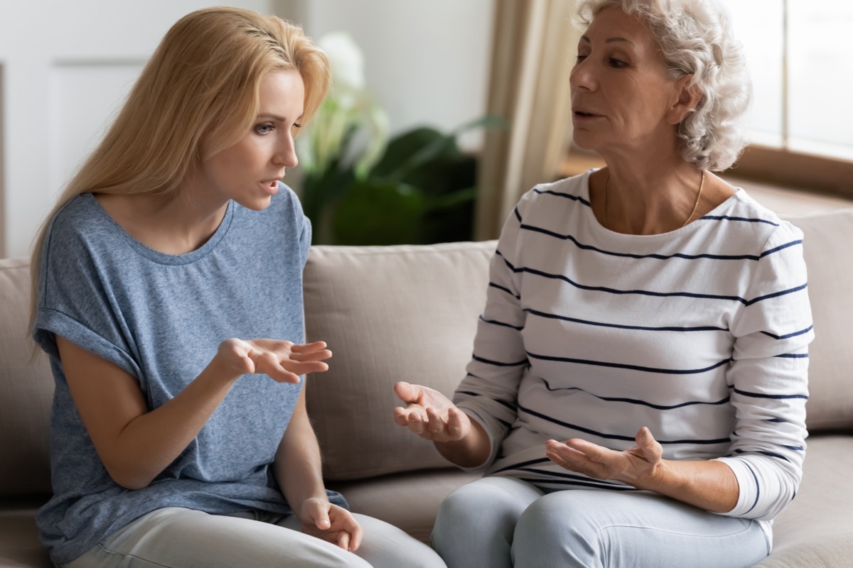 Stressed young blonde grown up daughter arguing with nervous old mature mother, sitting together at home. Irritated elderly woman lecturing adult child, different generations misunderstanding gap.