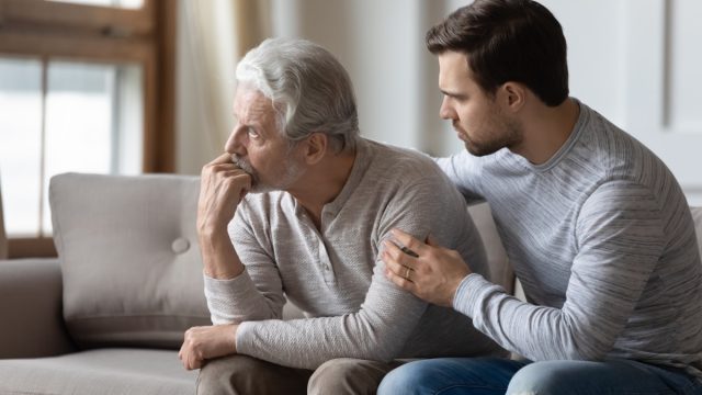 Loving young man embrace comfort upset elderly gray-haired dad suffering from depression or problems, caring adult grown-up son hug caress support mature father feeling lonely distressed at home