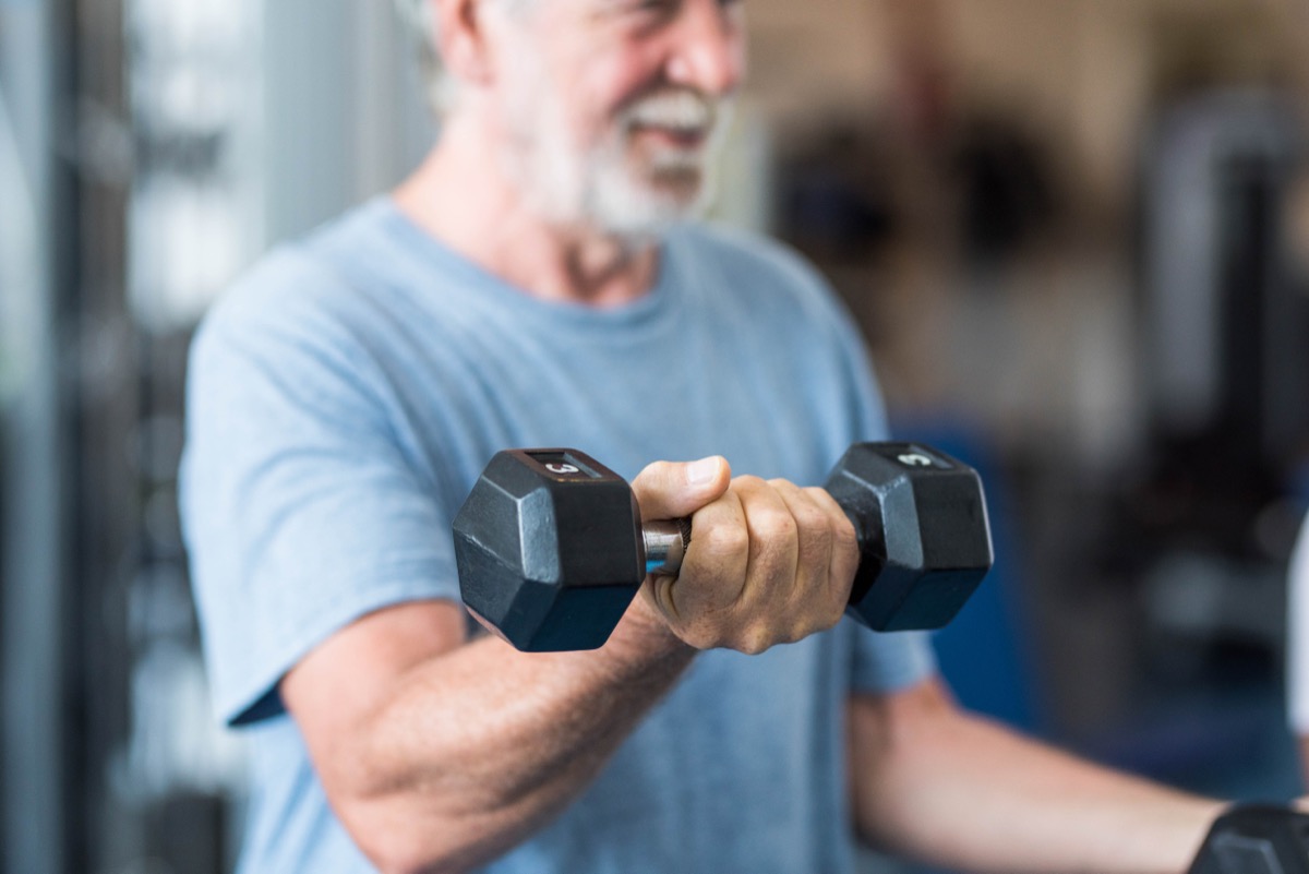 close up of mature man holding two dumbbells doing exercises at the gym