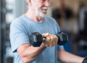 close up of mature man holding two dumbbells doing exercise at the gym to be healthy and fitness - portrait of active senior lifting weight