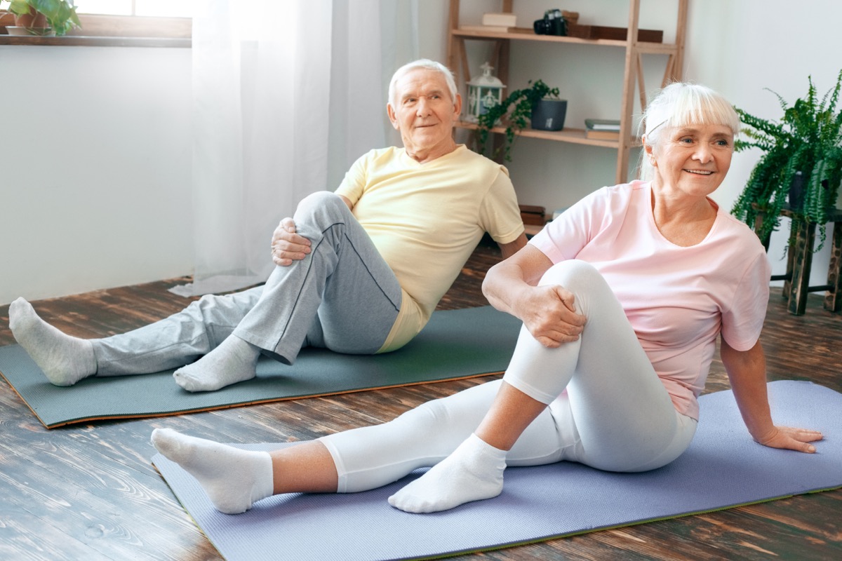 Senior couple doing yoga together at home health care leg stretching