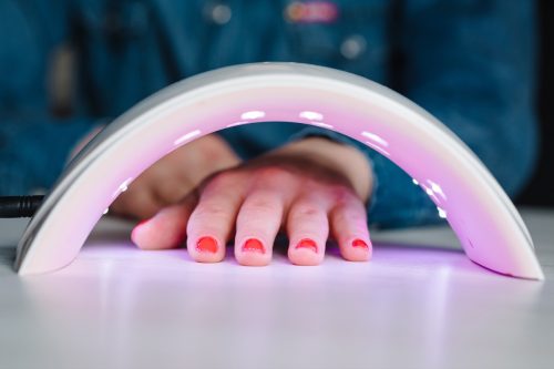 UV lamp with light for drying nails with gel polish. Woman hand inside lamp for nails on table close up. Red nails dried in the lamp. Girl makes a manicure at home, doing manicure herself, draws.