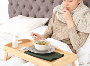 Sick young woman eating broth to cure cold in bed at home