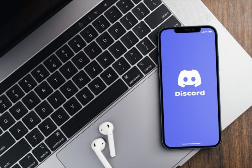 Discord app on smartphone laying on laptop along with airpods