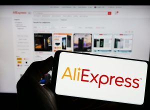 Person holding mobile phone with logo of Chinese c-commerce company AliExpress on screen in front of business web page.