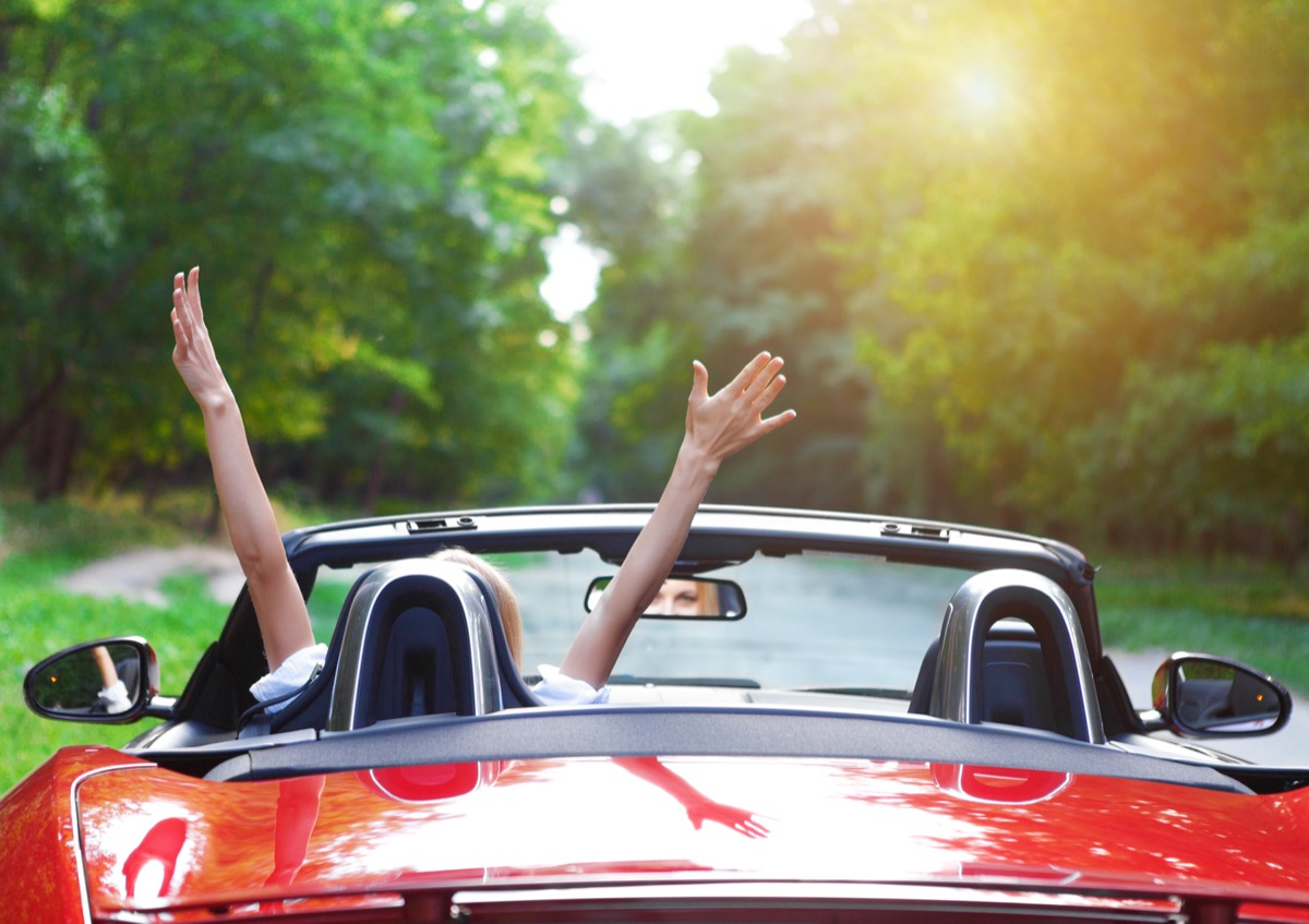 woman with her hands in the air while driving a sports car