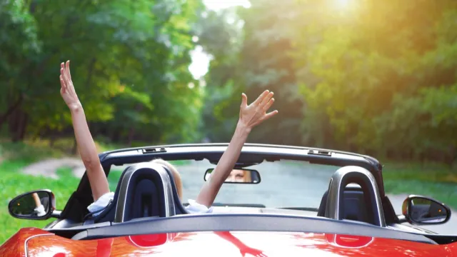 woman with her hands in the air while driving a sports car