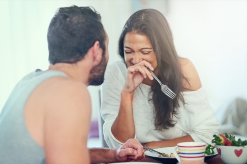 man and woman joking around while eating breakfast and laughing