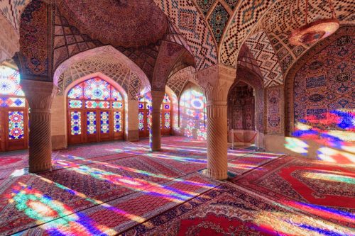 view of morning sunlight reflected through colorful stained glass windows on the wall and the floor of prayer hall at the Nasir al-Mulk Mosque 