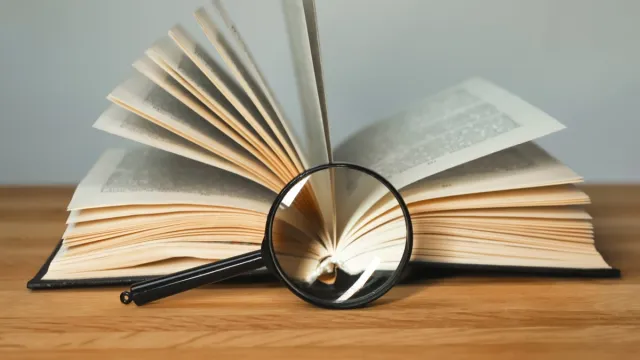 Magnifying glass and open books with turning pages on wood table.