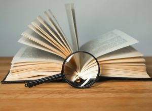Magnifying glass and open books with turning pages on wood table.
