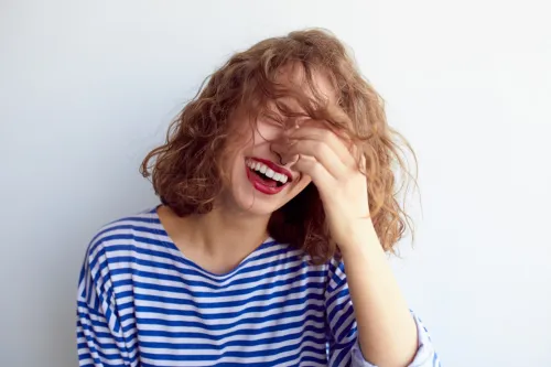 Laughing woman in marine shirt with curly hair over white wall.