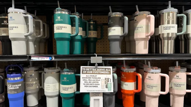 A display of colorful Stanley Tumblers on store shelves with a sign about purchase limits.