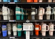 A display of colorful Stanley Tumblers on store shelves with a sign about purchase limits.