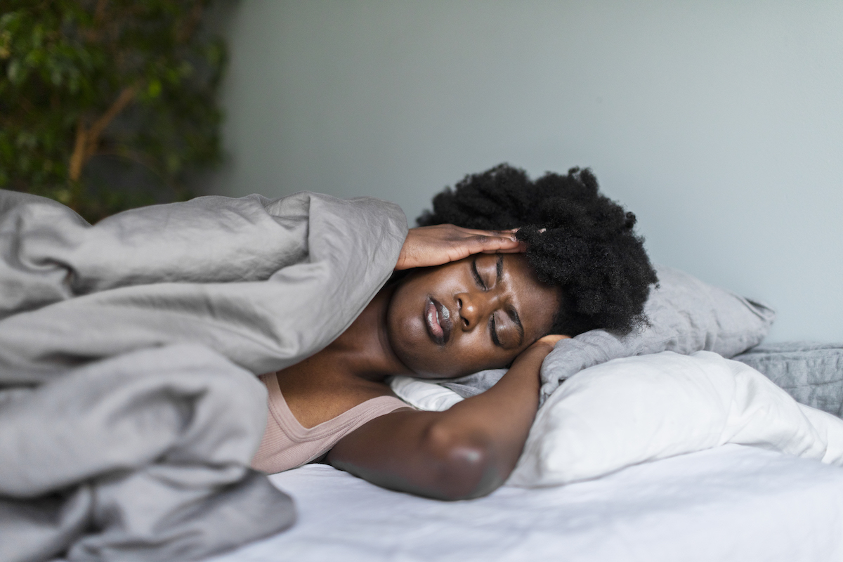 A distressed-looking woman laying in bed, holding her head, possibly having a nightmare.