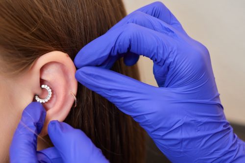 Hands wearing latex gloves are changing a diamond daith ear piercing on a woman