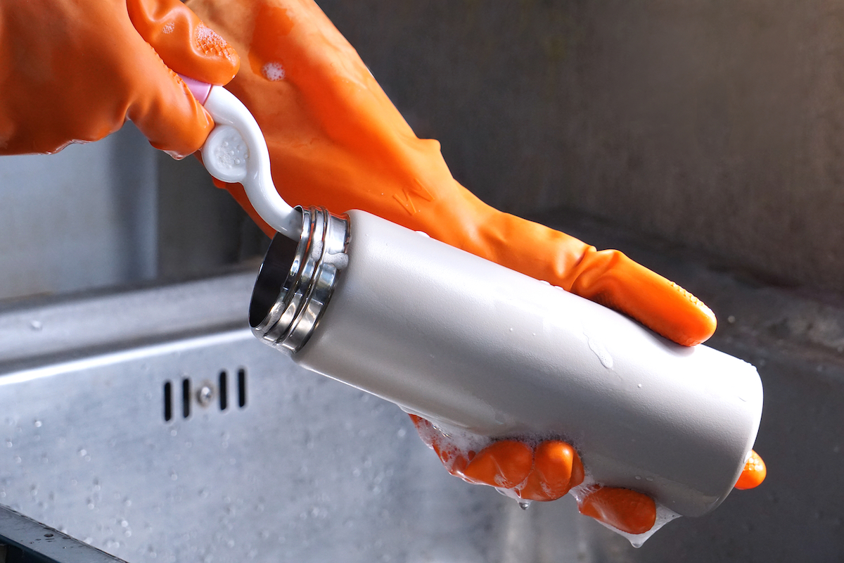 Close up of a person's hands in orange gloves washing a reusable water bottle