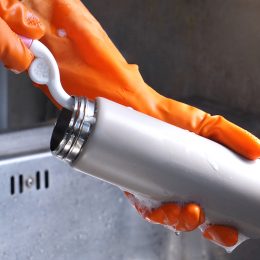 Close up of a person's hands in orange gloves washing a reusable water bottle