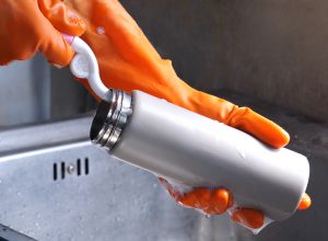 Close up of a person's hands in orange gloves washing a reusable water bottle