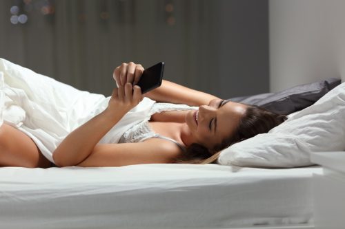 Happy woman flirting online on the bed in the night