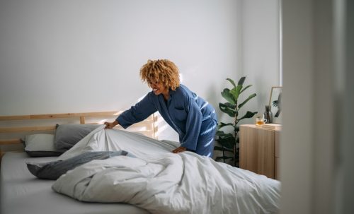 woman in pajamas making bed after waking up in her bedroom.