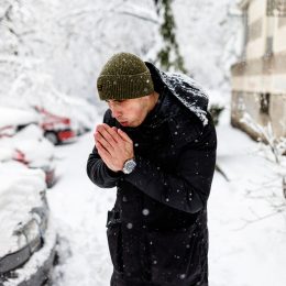A man trying to warm his hands while standing outside in a snow storm