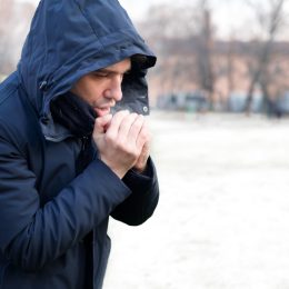 A man blowing onto his hands to warm them up while standing outside in cold weather