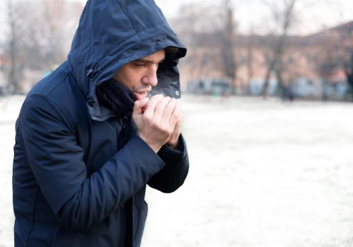 A man blowing onto his hands to warm them up while standing outside in cold weather