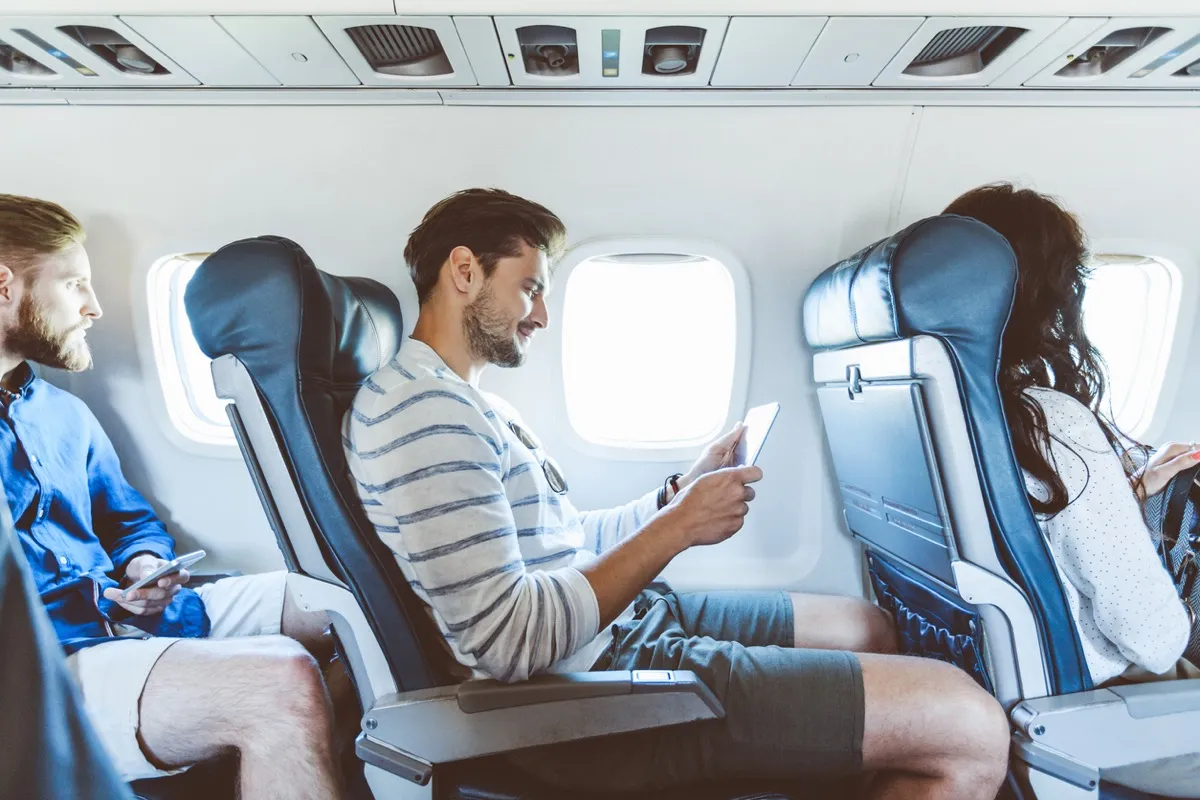 Young man sitting inside an airplane and using a digital tablet. 