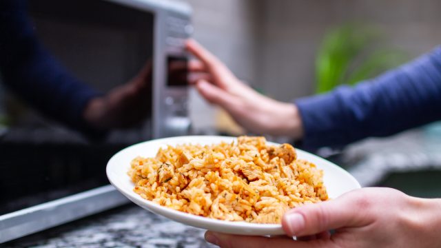 Close up of a person about to put a plate of rice in the microwave.