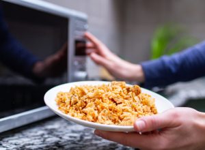 Close up of a person about to put a plate of rice in the microwave.