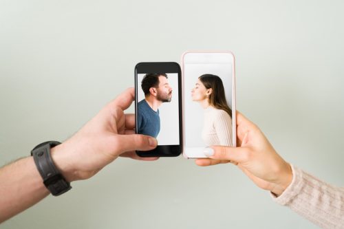 close up of hands holding smartphones next to one another, one containing a photo of a man while the other contains a photo of a woman