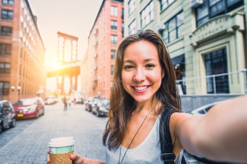 woman taking a selfie on the streets of new york city, holding coffee fup