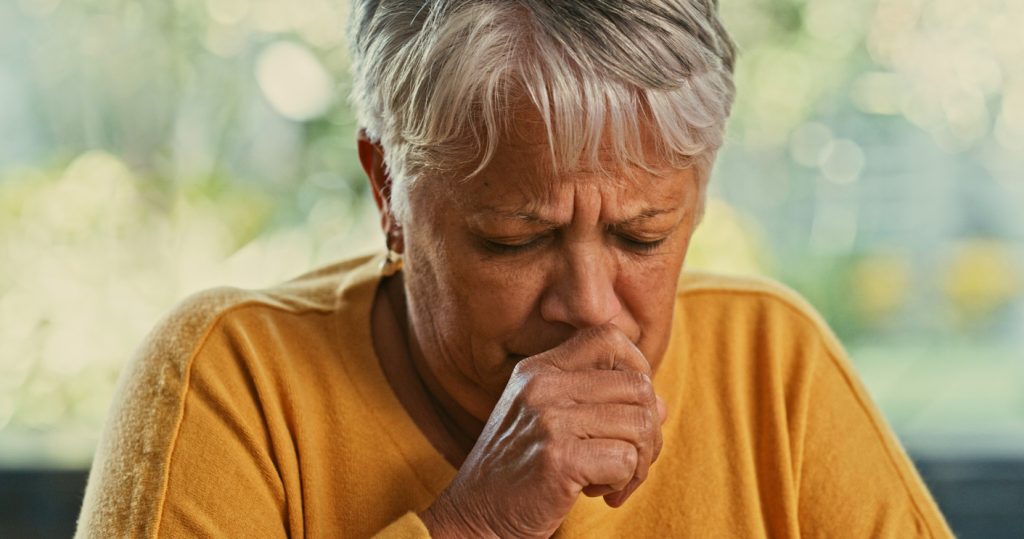 A senior woman coughing into her hand