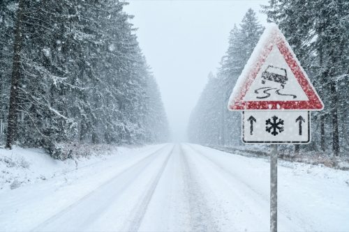 road covered in snow with road sign warning of slippery conditions