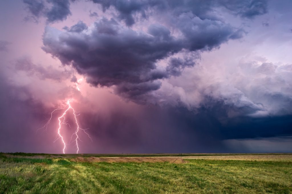 A thunderstorm over grassland with a lightning bolt.