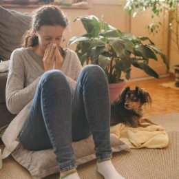 sick woman with tissues sitting on a pillow on the floor next to her dog
