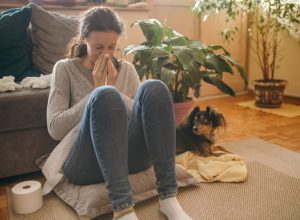 sick woman with tissues sitting on a pillow on the floor next to her dog